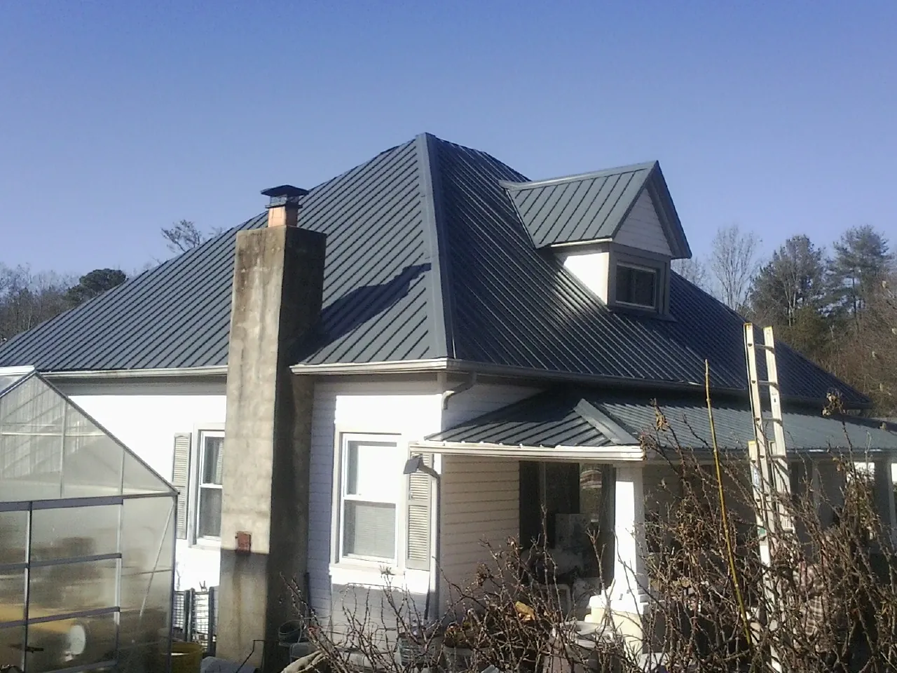 Dark blue standing seam metal roof on a white farmhouse with dormer — Slate & Tile Roof Repair by Roofing Brothers in Malmo