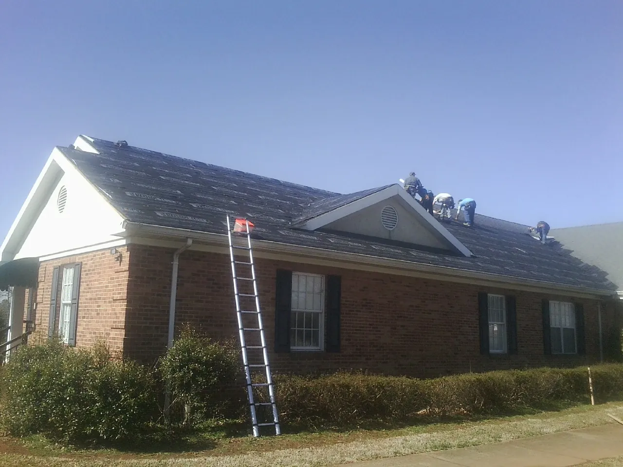 Crew tearing shingles off a brick ranch roof with a ladder set — Metal Roof Repair work by our crew in Malmo