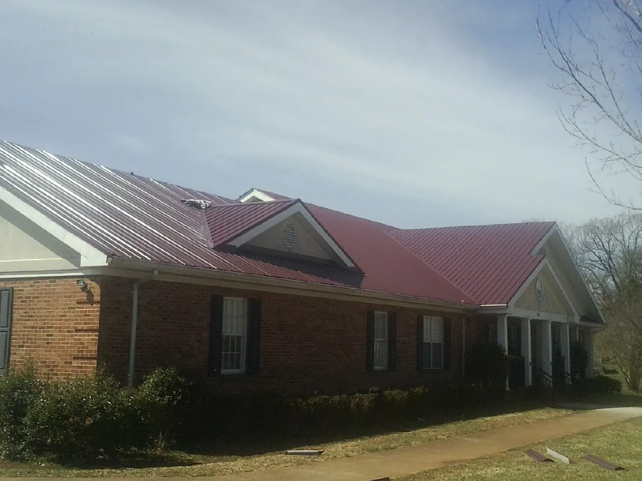 Red metal roof with gabled entries on a long brick building, from a Hail Damage Roof Repair job in Malmo