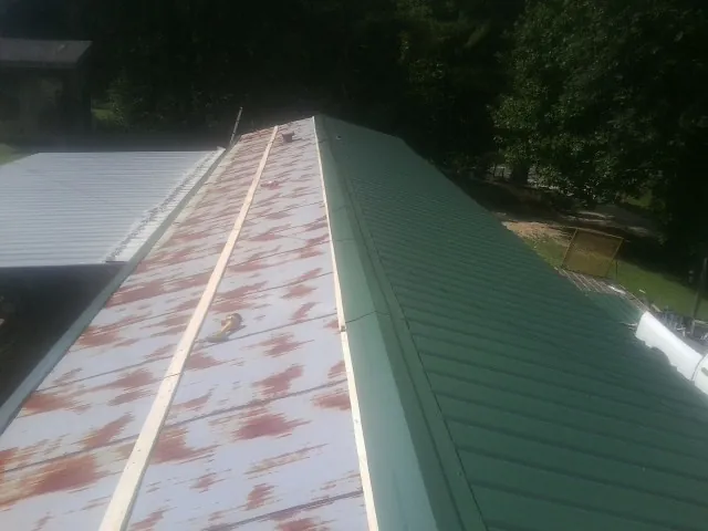 Old rusted panels beside newly installed green metal roofing — Wind Damage Roof Repair by Roofing Brothers in Malmo